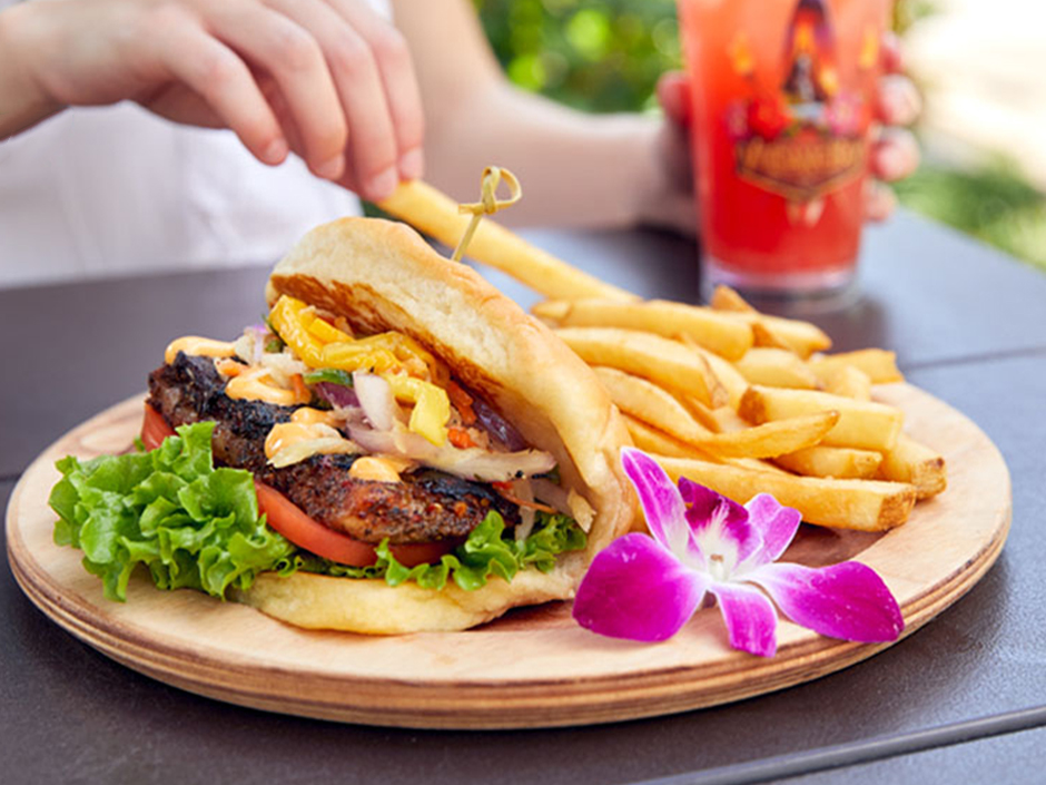 A hand reaching for a fry next to a Jerk Mahi Sandwich