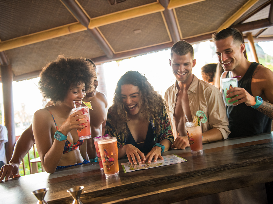A group of friends smile around their drinks at the Dancing Dragons Boat Bar in Volcano Bay