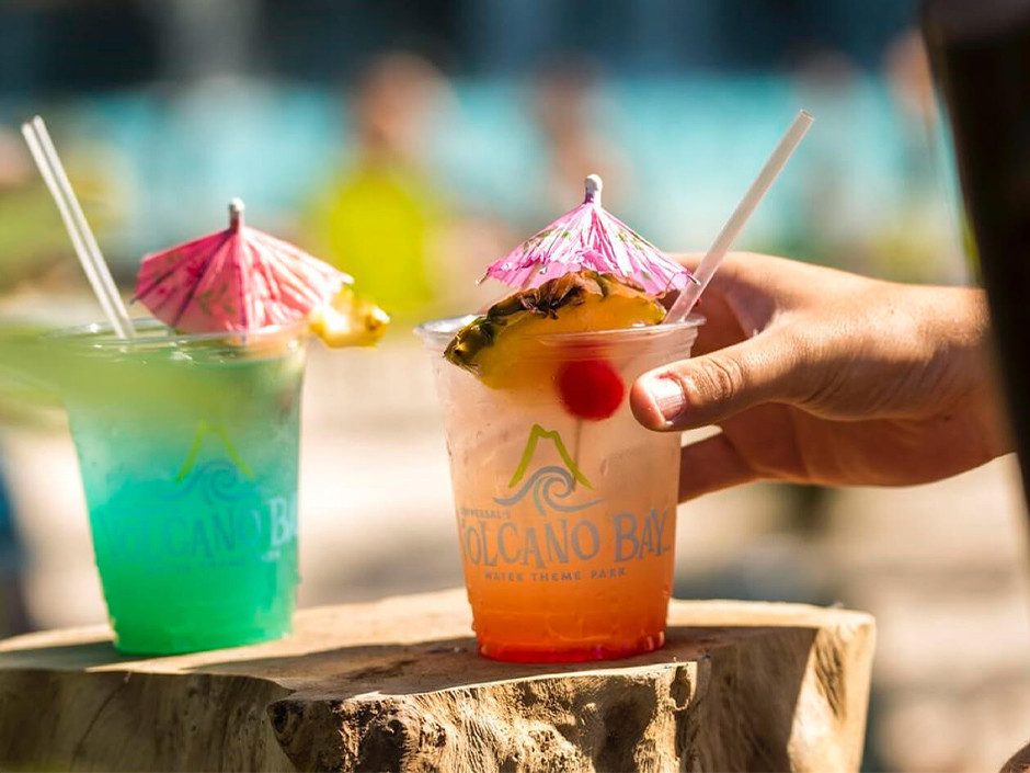 A hand reaches into the frame and picks up a cocktail on Waturi Beach at Volcano Bay