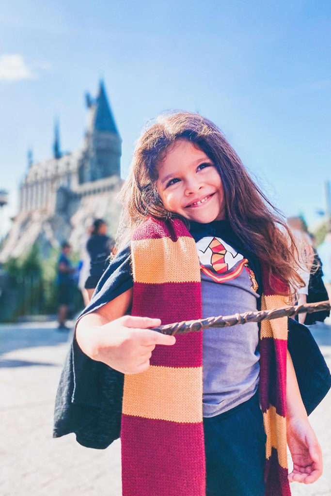 Little Girl with Gryffindor scarf holding wand in front of Hogwarts Castle