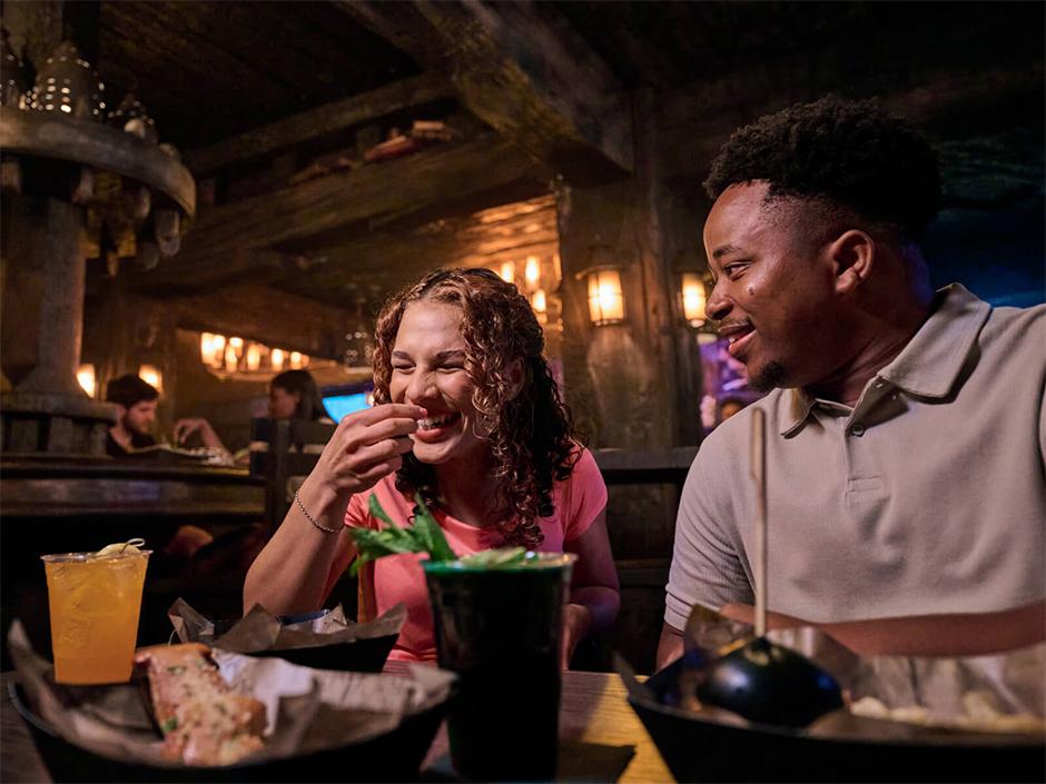 Two friends smile and enjoy a meal in The Burning Blade Tavern in Dark Universe