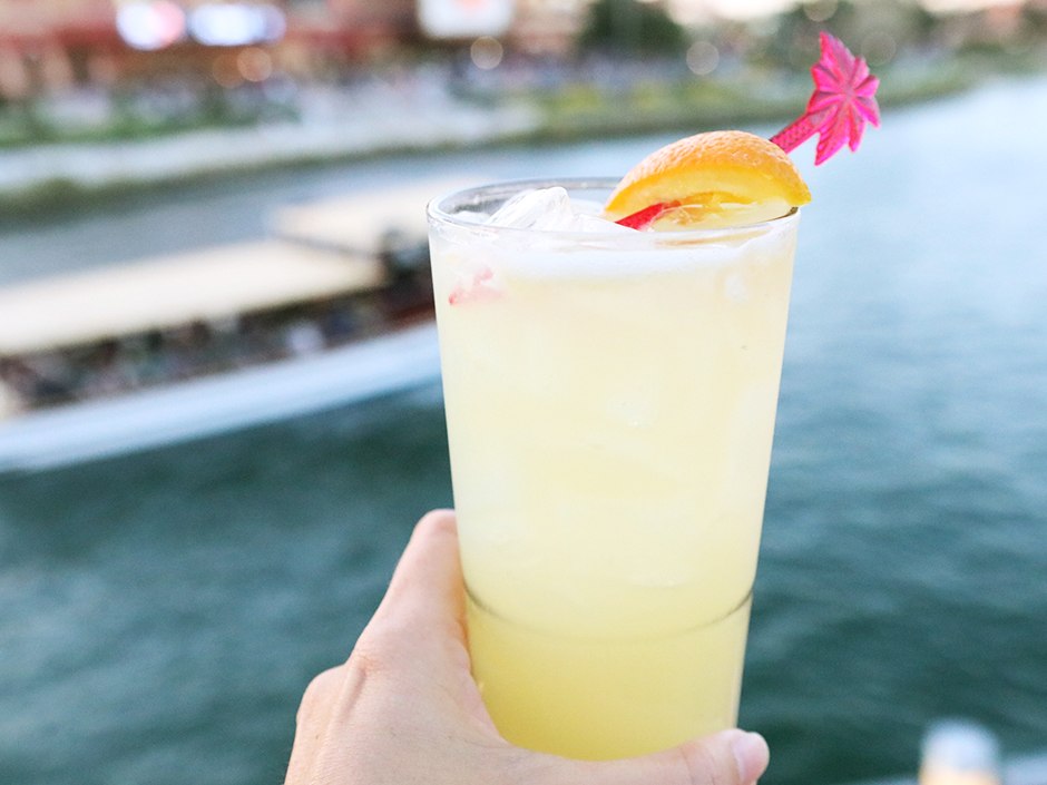 Hand holding out Mango Margarita with Water Taxi in the background