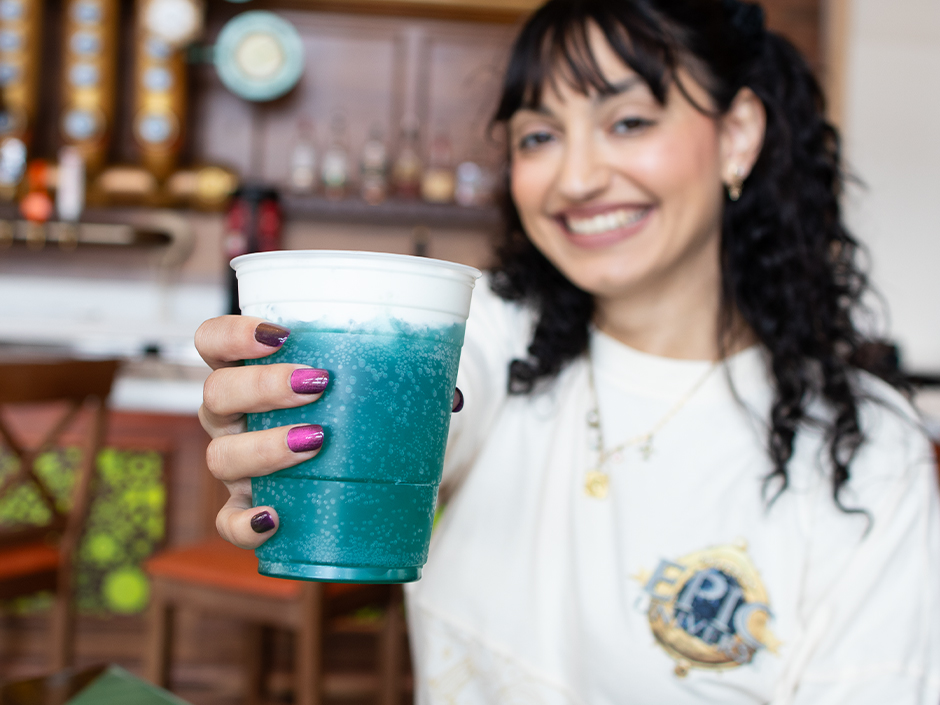 A guest smiles and holds a First Light Mocktail toward the camera inside Meteor Astropub