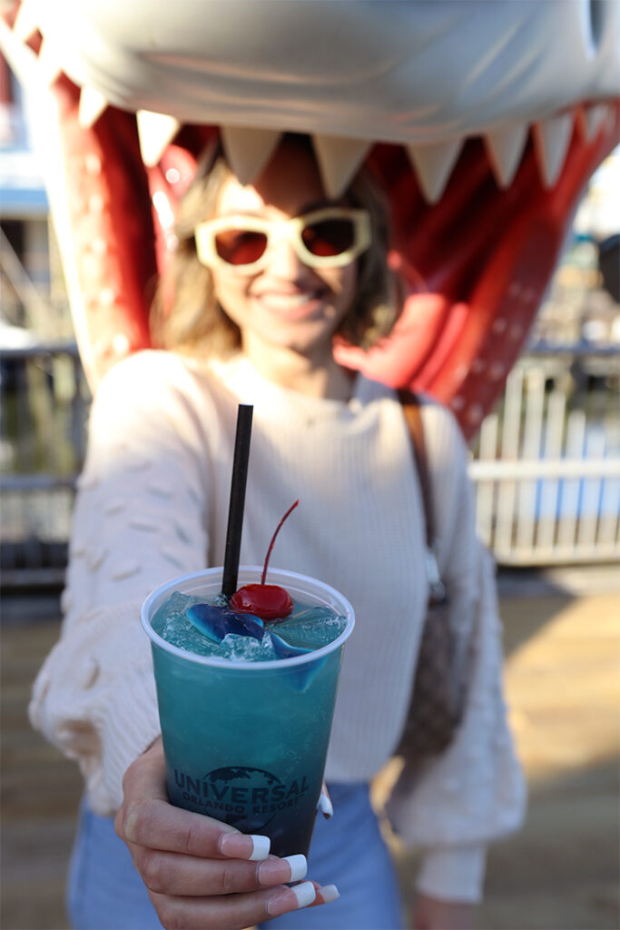 Woman inside mouth of Jaws shark holding out blue mocktail drink