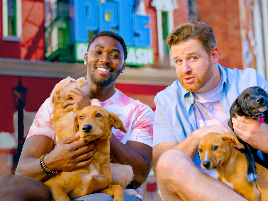 Two men, The Ride Guys, are holding puppies in front of The Secret Life of Pets attraction at Universal Studios Hollywood