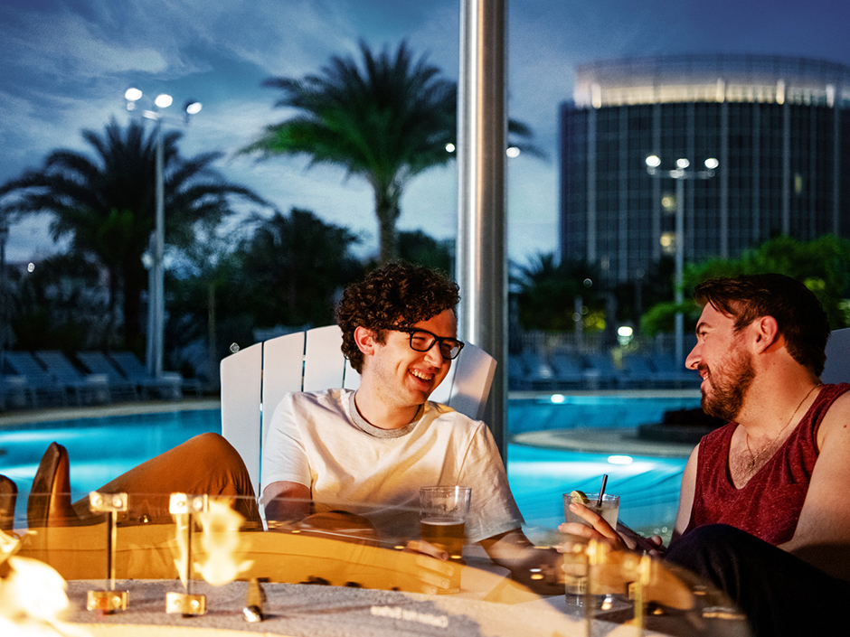 Two people sitting by outdoor fireplace with Aventura hotel in the background