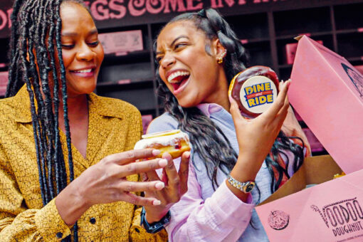 Two women enjoying doughnuts from a pink box at Universal from Voodoo Doughnuts
