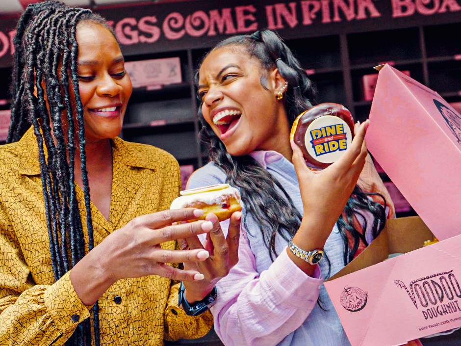 Two women enjoying doughnuts from a pink box at Universal from Voodoo Doughnuts