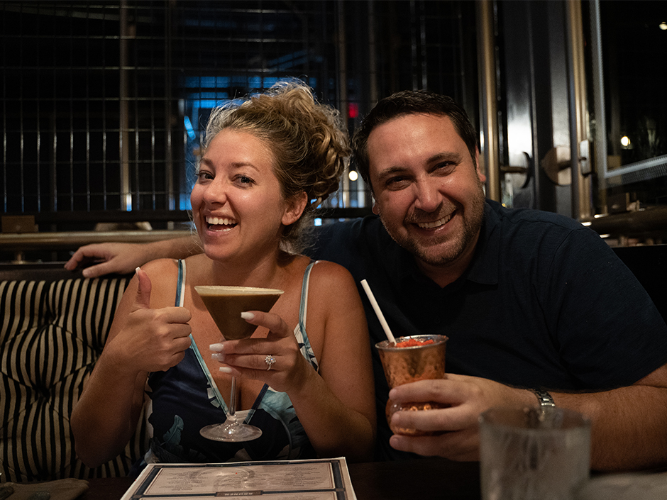 A man and a woman holding cocktails inside of a restaurant