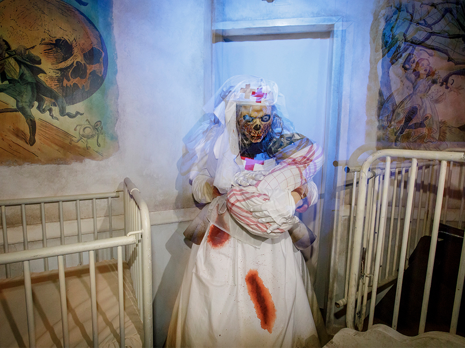 Demon nurse holds skeletal baby next to crib