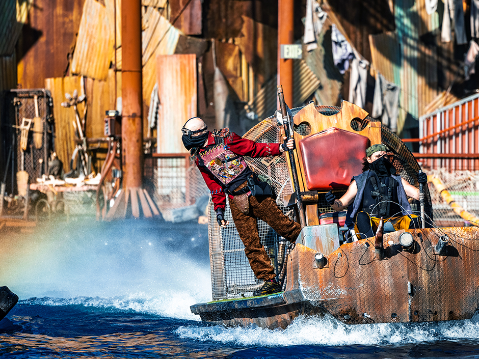 Man leans off of large flatbed boat made of rusty metal at the WaterWorld show at Universal Studios Hollywood.
