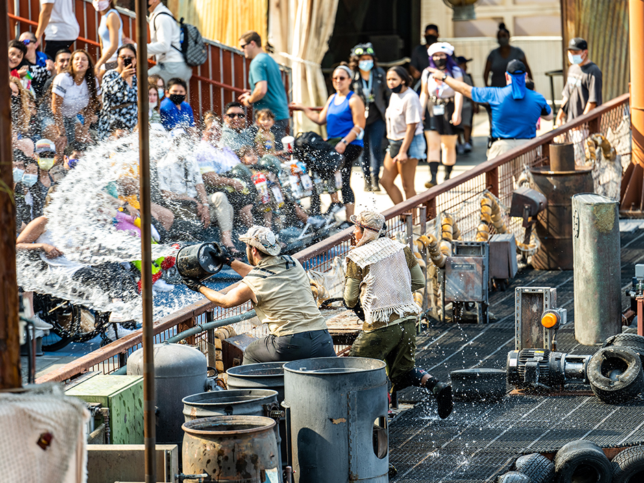 At the WaterWorld show, two men in fishing gear throw buckets of water on Universal Studios Hollywood guests in bleachers.