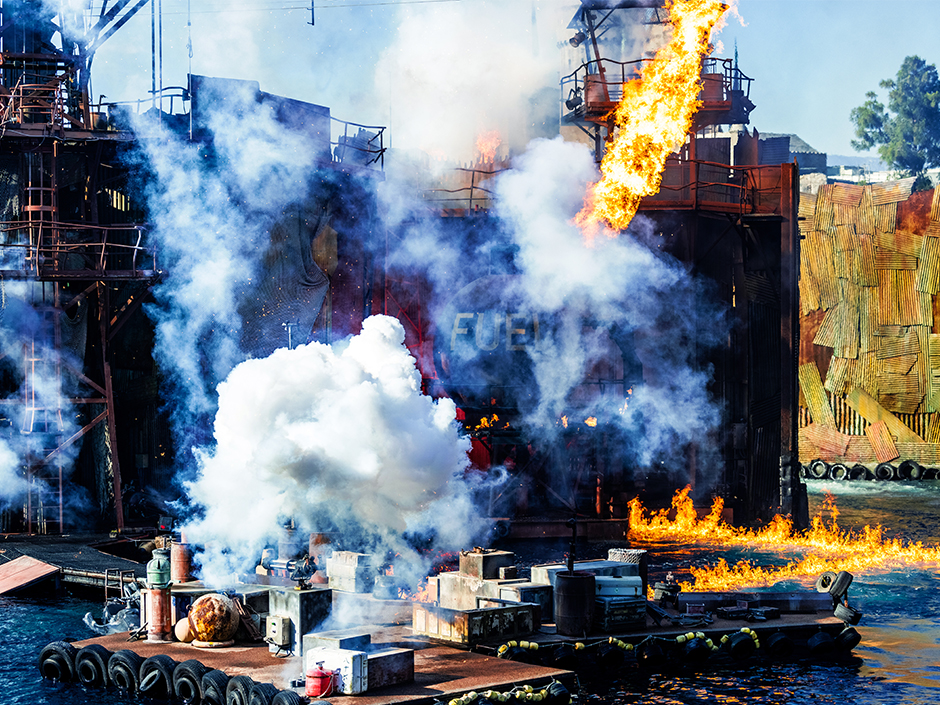 Wide shot of an explosion on a large scrap metal structure floating on water at the WaterWorld show at Universal Studios Hollywood.
