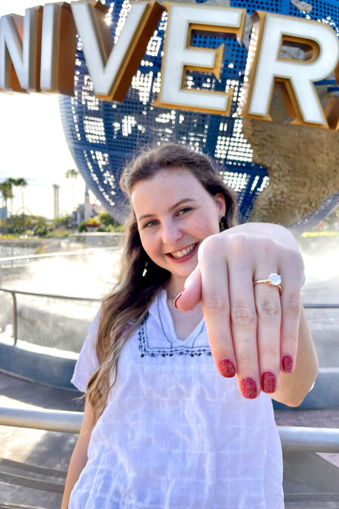 A woman stands in front of the Universal Orlando globe showing off her ring