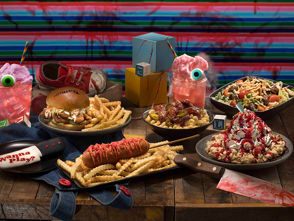 A spread of Chucky-themed food and drinks for Halloween Horror Nights, including a corndog, a fried chicken sandwich, and a knife-shaped cookie.