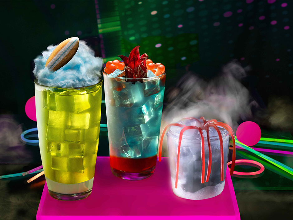 Three Halloween Horror Nights cocktails based on Stranger Things, including a yellow cocktail with a candy surfboard on it.