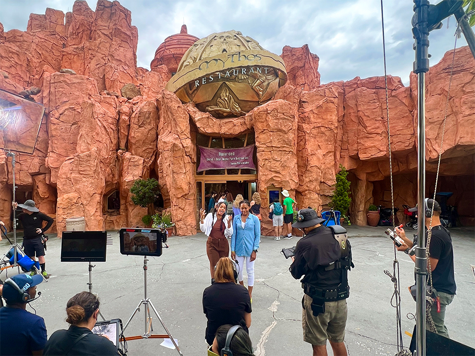 Two girls stand in front of Mythos Restaurant with a film crew