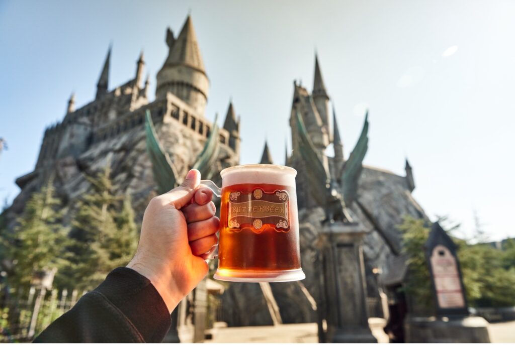 A mug of butterbeer in front of Hogwarts castle.