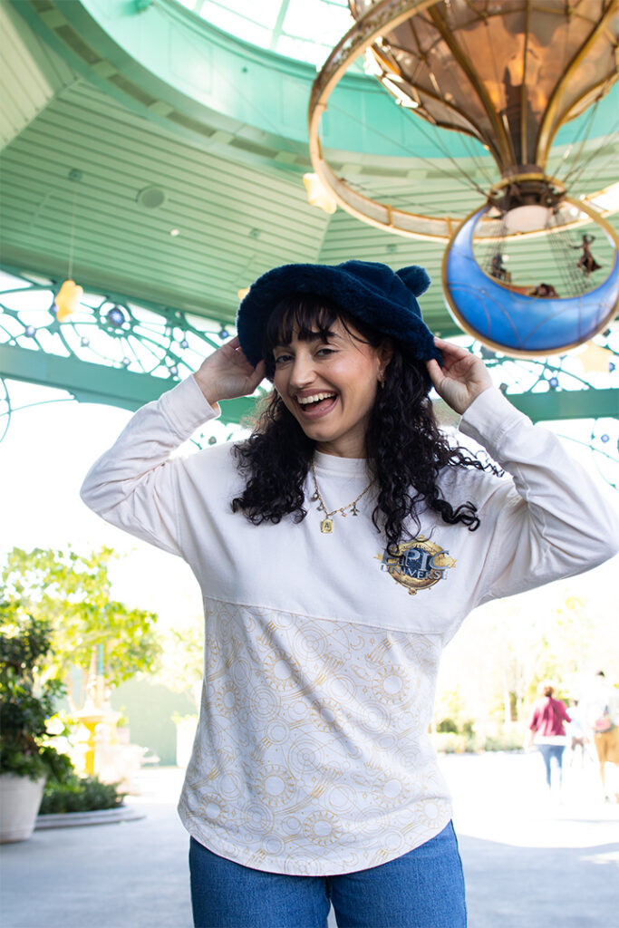 A guest poses in a Captain Cacao bucket hat near Moonship Chocolates and Celestial Sweets in Epic Universe