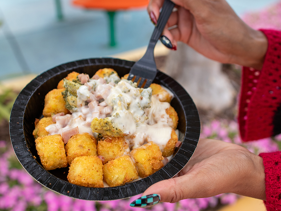 Hands holding a fork and bowl of Green Eggs and Ham Tots in Seuss Landing.