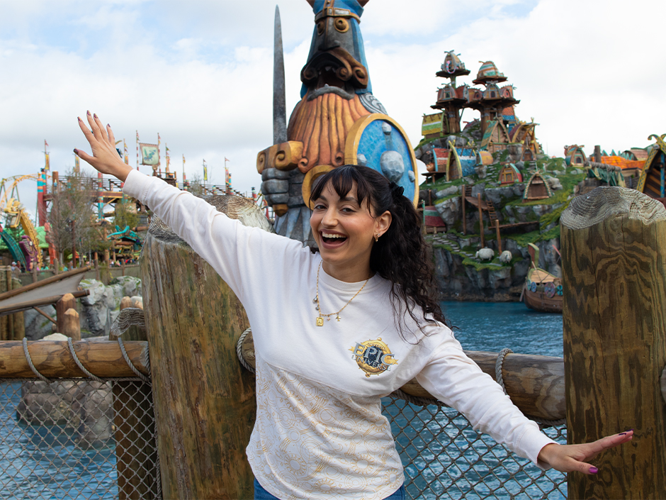 A guest spreads their arms like a dragon's wings and poses for a photo near the entrance of How to Train Your Dragon - Isle of Berk at Epic Universe