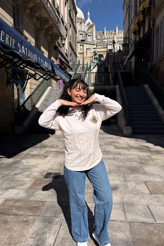 A guest poses in front of a scenic alleyway in The Wizarding World of Harry Potter - Ministry of Magic in Epic Universe