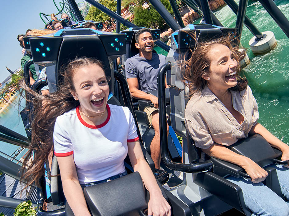Two Caucasian women and a brown man smiling and riding the VelociCoaster.