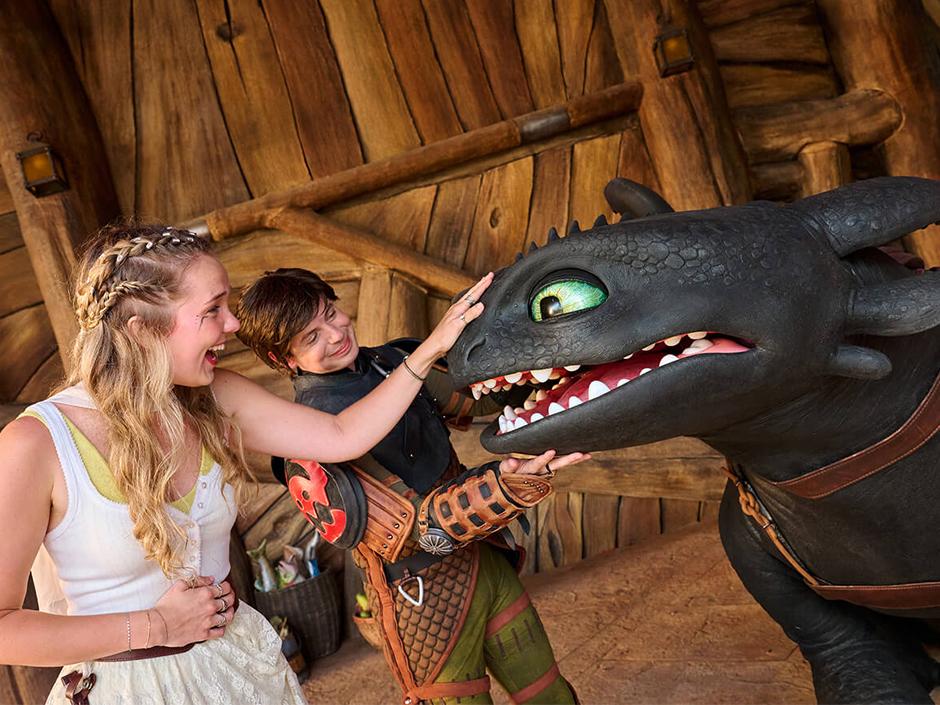 A girl pets Toothless while standing next to Hiccup in How to Train Your Dragon - Isle of Berk