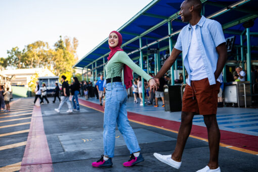 A woman wearing a head scarf holding hands and walking with an African American man.