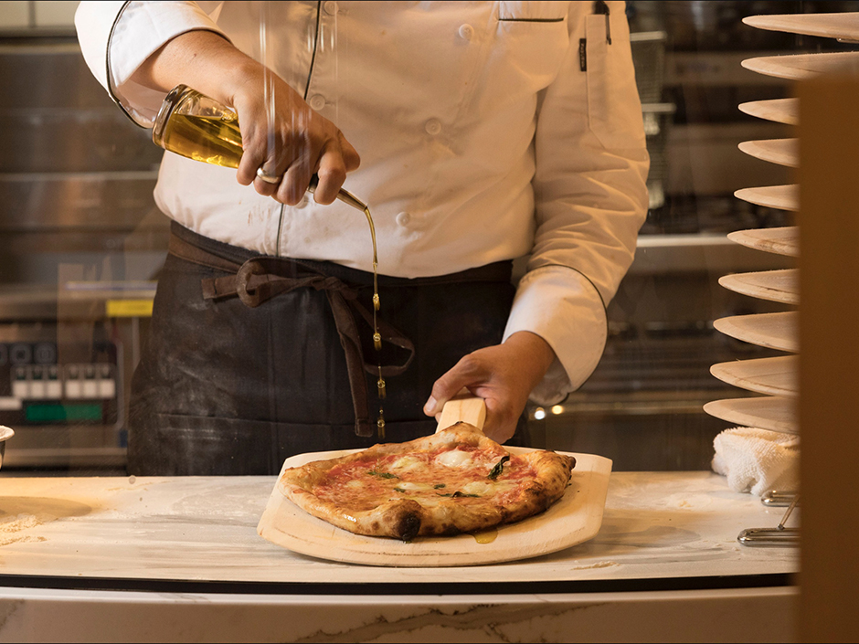 A chef pouring olive oil on a pizza.