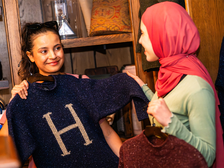 A woman shows her friend a blue knit sweater with an H on it in Wizarding World of Harry Potter.