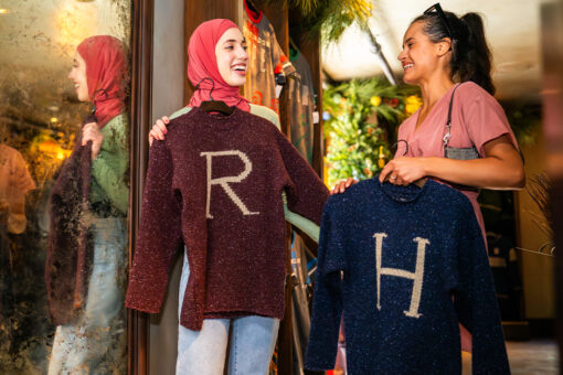 Two woman hold knitted sweaters, one with an R on it and the other with an H, in the Wizarding World of Harry Potter.