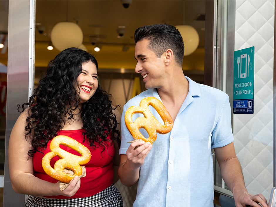 Two guests holding pretzels in the shape of "60", menu items for the 60th Anniversary of the Studio Tour.