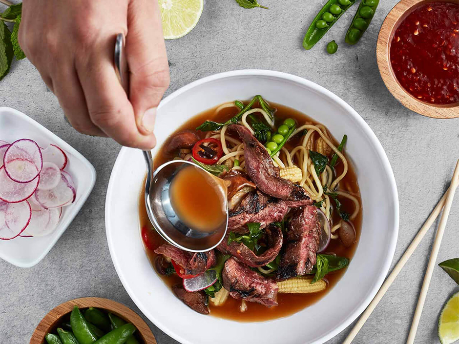 A bowl of ramen with someone scooping broth.