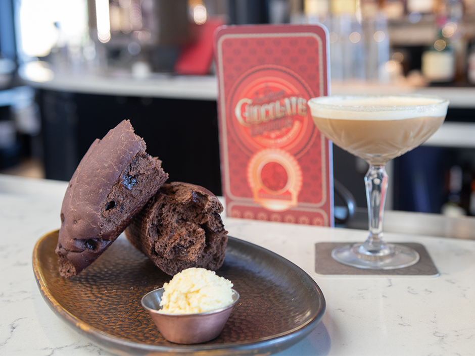 Toothsome's chocolate bread split in half on a copper plate with a menu and mocktail in the background.