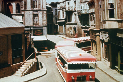 An old photo of a red and white striped tram traversing the "Little Europe" section of the Universal backlot.