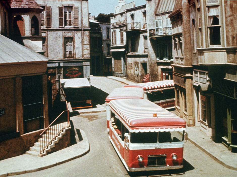 An old photo of a red and white striped tram traversing the "Little Europe" section of the Universal backlot.