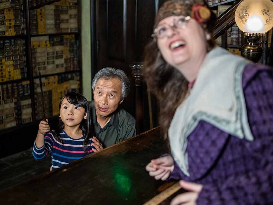 A young girl points a wand outside of view insider Ollivanders Wand Shop.