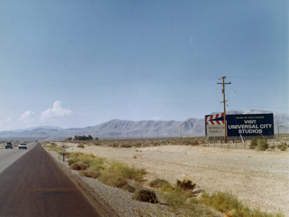 A long empty road in California, with a billboard reading "VISIT UNIVERSAL CITY STUDIOS."