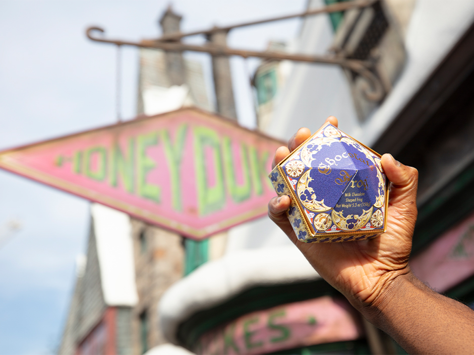 A guest holds up a chocolate frog box outside of Honeydukes at The Wizarding World of Harry Potter.