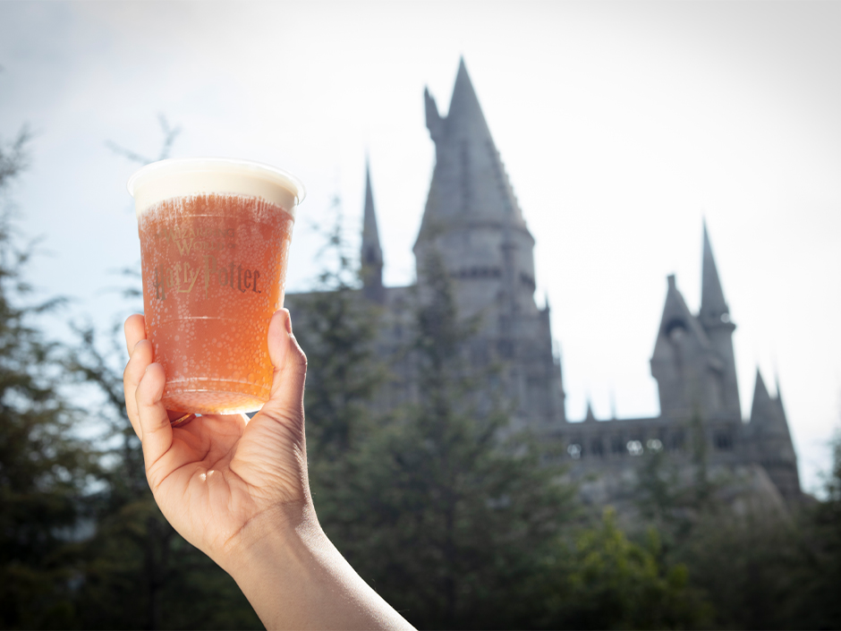 Cold Butterbeer held up in front of Hogwarts Castle in the Wizarding World of Harry Potter.