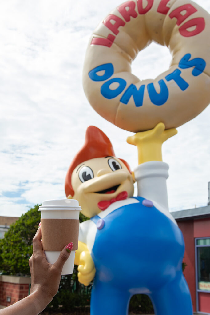 Coffee held up in front of Lard Lad Donuts in Springfield USA