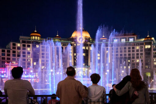 Guest watch the Epic Universe fountain show at night in front of Helios Grand Hotel