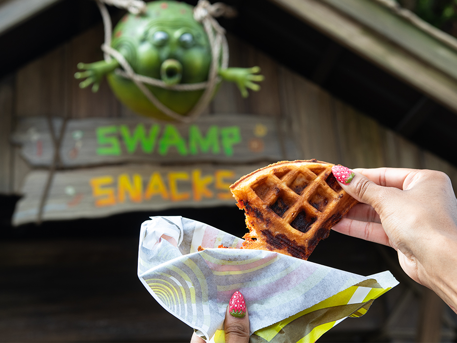 A hand holding up a Far Far A Waffle in front of Swamp Snacks