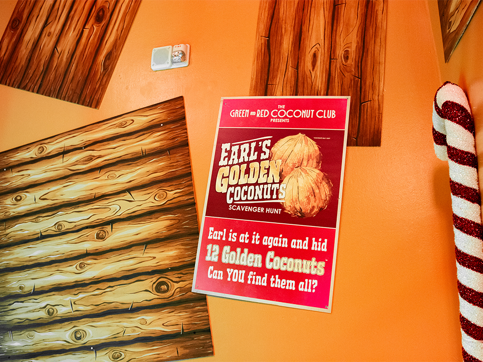 Wood panels on a wall with a sign that reads: The Green & Red Coconut Club Presents Earl's Golden Coconuts Scavenger Hunt. Earl is at it again and hid 12 Golden Coconuts. Can YOU find them all?