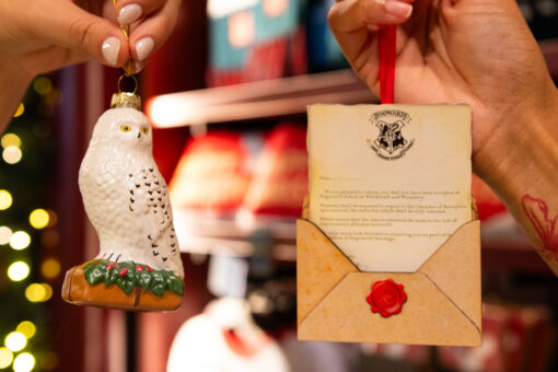 Two hands holding Harry Potter Christmas ornaments of Hedwig and a Hogwarts acceptance letter