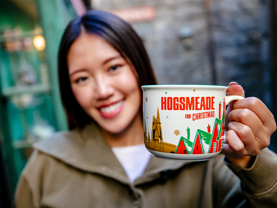 A guest holds up a mug reading "Hogsmeade for Christmas" in The Wizarding World of Harry Potter.