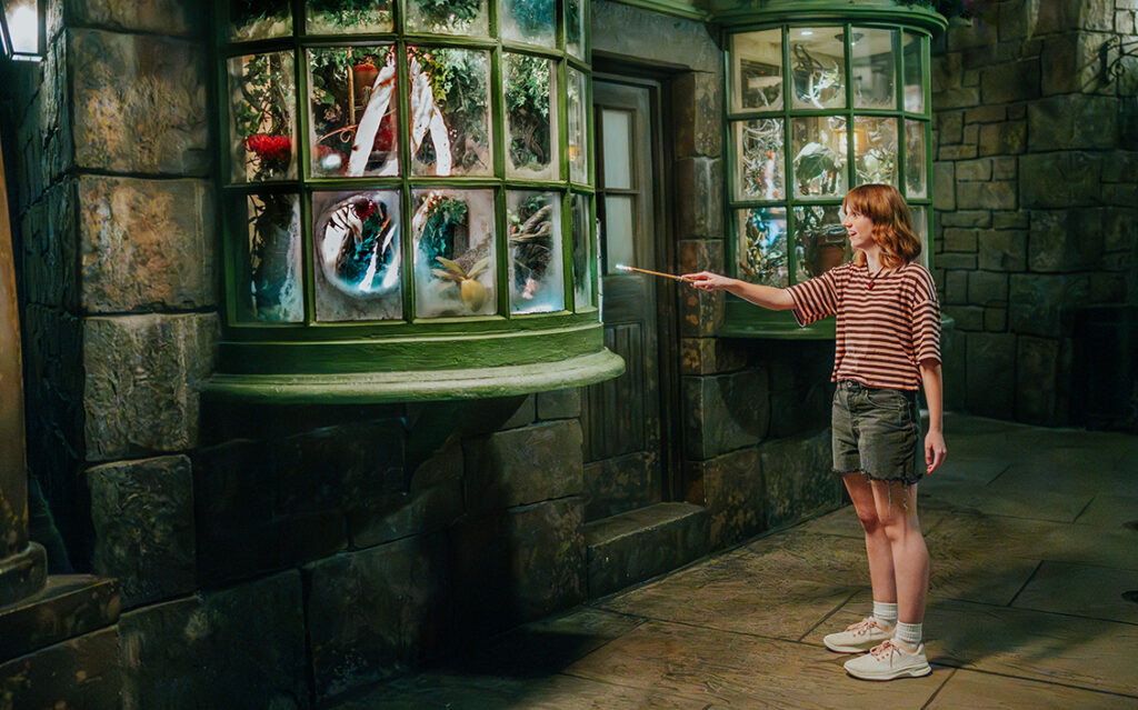 A young girl casts a spell with a 2nd Generation Interactive Wand in The Wizarding World of Harry Potter - Hogsmeade