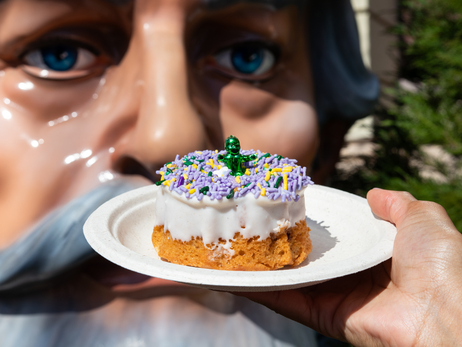 A King Cake on a plate in front of the King Statue at Universal Mardi Gras