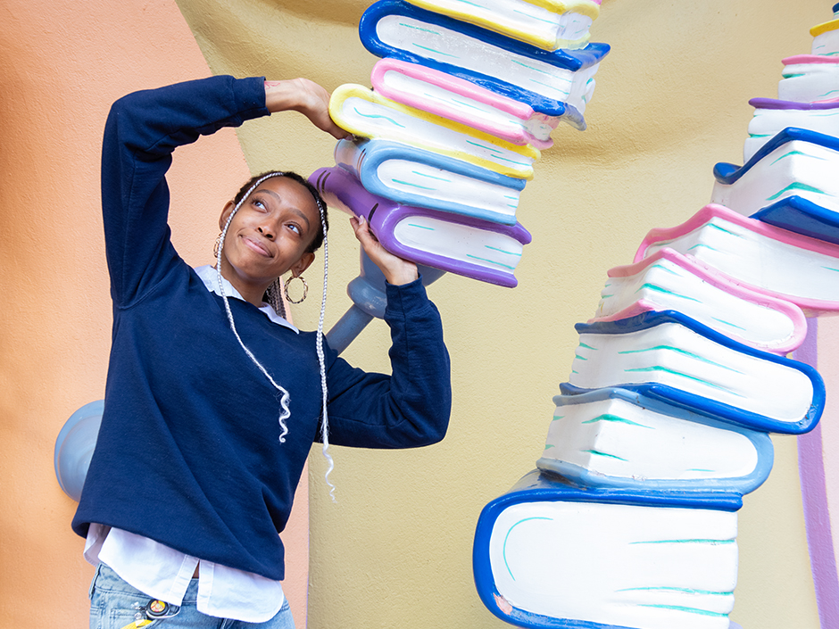 A girl stands under a stack of books outside of All the Books You Can Read